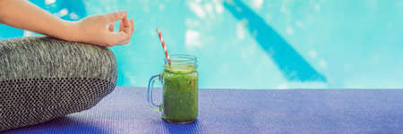 Closeup of a woman's hands during meditation with a green smoothies of spinach, orange and banana on the background of the pool. BANNER, long formatの写真素材