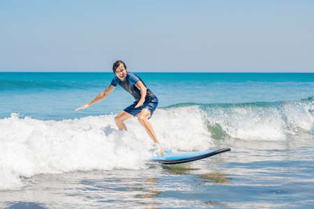 Young man, beginner Surfer learns to surf on a sea foam on the Bali island.の写真素材