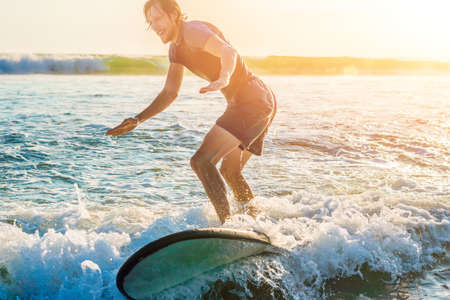Young man, beginner Surfer learns to surf on a sea foam on the Bali island.の写真素材