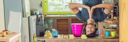 A man stands on his hands upside down in the kitchen. BANNER, long format