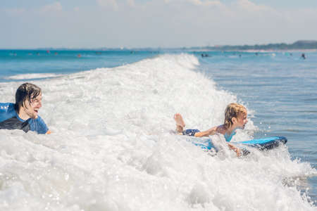 Father teaching his young son how to surf in the sea on vacation or holiday. Travel and sports with...