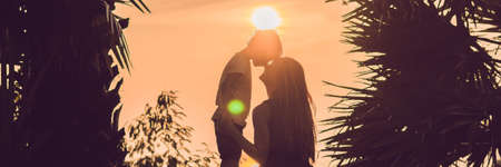 Silhouettes of mother and son, who meet the sunset in the tropics against the backdrop of palm trees. BANNER, long formatの写真素材