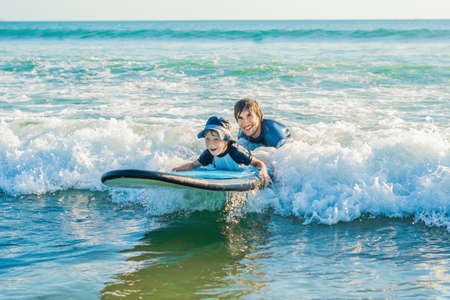 Father teaching his young son how to surf in the sea on vacation or holiday. Travel and sports with...