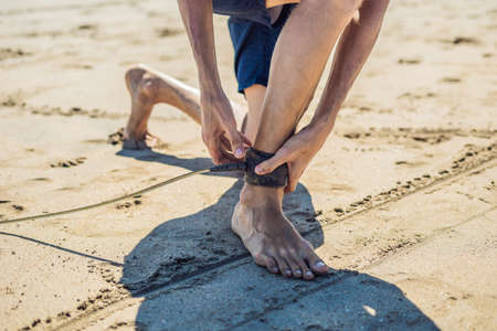 Young man surfer getting on the surfboard's leash.の写真素材