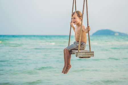 Happy boy sit on swing at the sea shore on sunset.の写真素材