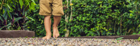 Boy Walking On A Textured Cobble Pavement, Reflexology. Pebble stones on the pavement for foot reflexology. BANNER long formatの写真素材