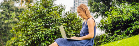 Young smart student female in casual clothes. Woman sitting on grass ground, working on laptop pc...