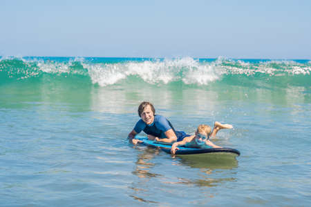 Father teaching his young son how to surf in the sea on vacation or holiday. Travel and sports with...