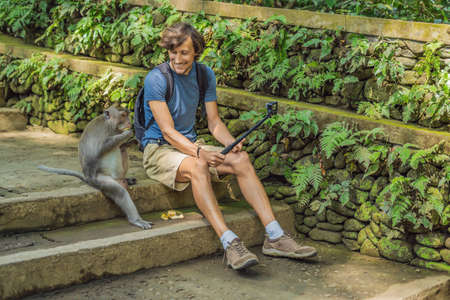 Selfie with monkeys. Young man uses a selfie stick to take a photo or video blog with cute funny...