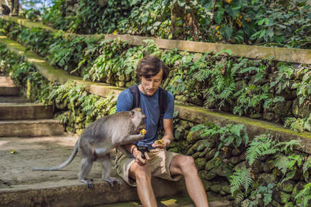Selfie with monkeys. Young man uses a selfie stick to take a photo or video blog with cute funny...