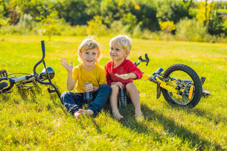 Two little boys drink water in the park after riding a bike.の写真素材