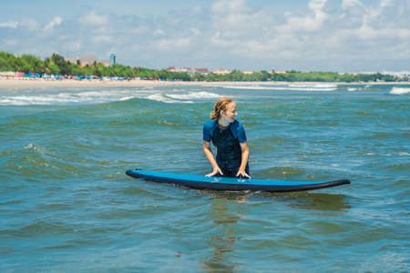 Joyful young woman beginner surfer with blue surf has fun on small sea waves.