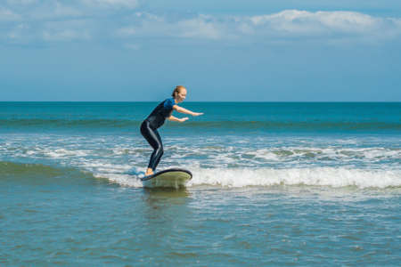 Joyful young woman beginner surfer with blue surf has fun on small sea waves.