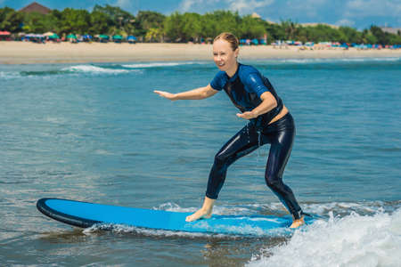 Joyful young woman beginner surfer with blue surf has fun on small sea waves.の写真素材