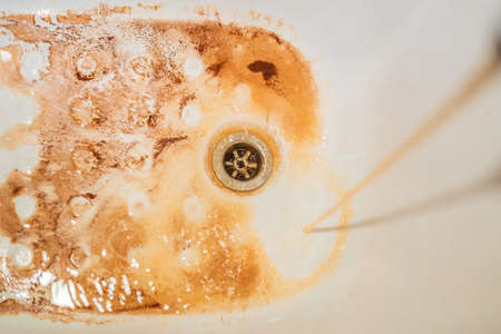 Dirty brown running water falling into a white sink from tap. Environmental pollution concept.の写真素材