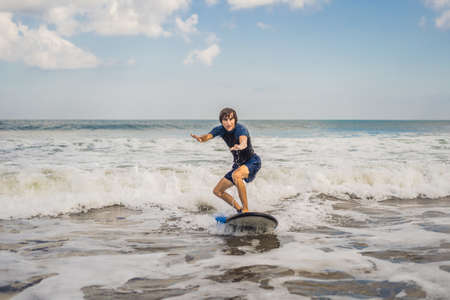 Young man, beginner Surfer learns to surf on a sea foam on the Bali island.
