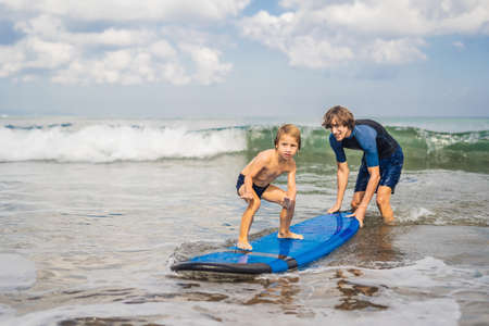 Father or instructor teaching his 4 year old son how to surf in the sea on vacation or holiday.の写真素材