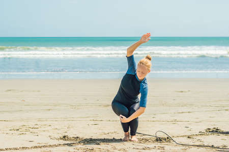 Young woman surfer warming up on the beach before surfing.の写真素材