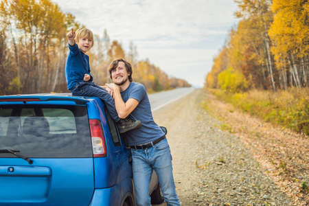 Dad and son are resting on the side of the road on a road trip. Road trip with children concept.の写真素材