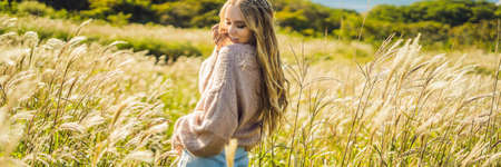 Young beautiful woman in autumn landscape with dry flowers, wheat spikes.