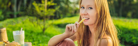 Young woman eats french fries and a hamburger in the outside cafe.の写真素材