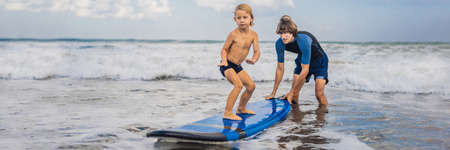 Father or instructor teaching his 4 year old son how to surf in the sea on vacation or holiday.の写真素材