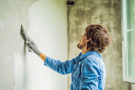 master is applying white putty on a wall and smearing by putty knife in a room of renovating house in daytime.の写真素材