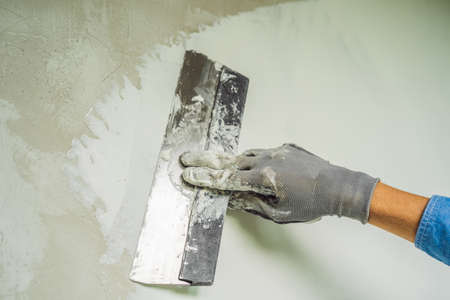 master is applying white putty on a wall and smearing by putty knife in a room of renovating house in daytime.の写真素材