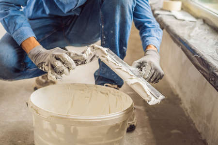 master is applying white putty on a wall and smearing by putty knife in a room of renovating house in daytime.の写真素材