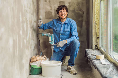 Young male painter kneads putty with water in a bucket using a hand-held mixer for building mixes.の写真素材