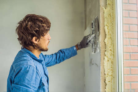 master is applying white putty on a wall and smearing by putty knife in a room of renovating house in daytime.の写真素材