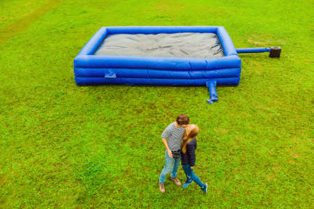 Young sexy couple on the background of a large inflatable blue trampoline on green grass.