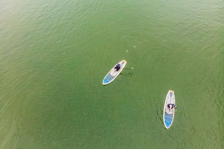 Strong men floating on a SUP boards in a beautiful bay on a sunny day. Aerial view of the men crosses the bay using the paddleboard. Water sports, competitions.の写真素材