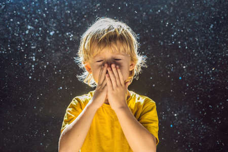 Allergy to dust.Boy sneezes because he is allergic to dust. Dust flies in the air backlit by light.の写真素材