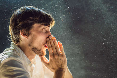 Allergy to dust. A man sneezes because he is allergic to dust. Dust flies in the air backlit by light.の写真素材