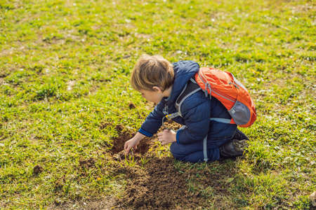 The boy plays recycling. He buries plastic disposable dishes and biodegradable dishes.