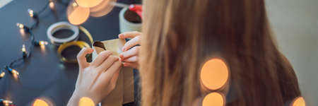 Young woman is packing presents. Present wrapped in craft paper with a red and gold ribbon for christmas, birthday, mothers day or valentineの写真素材