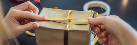 Young woman is packing presents. Present wrapped in craft paper with a red and gold ribbon for christmas, birthday, mothers day or valentineの写真素材