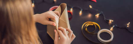 Young woman is packing presents. Present wrapped in craft paper with a red and gold ribbon for christmas, birthday, mothers day or valentineの写真素材