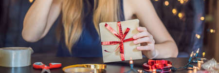 Young woman is packing presents. Present wrapped in craft paper with a red and gold ribbon for christmas, birthday, mother's day or valentine.の写真素材