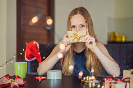 Young woman is packing presents. Present wrapped in craft paper with a red and gold ribbon for christmas or new year. Woman makes an advent calendar for her child.の写真素材