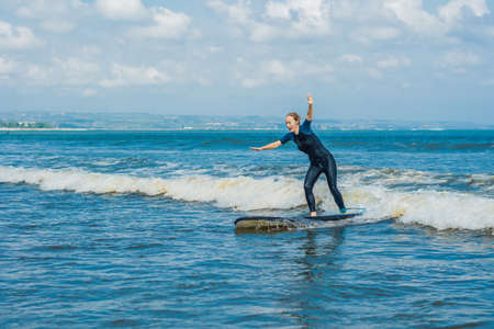 Joyful young woman beginner surfer with blue surf has fun on small sea waves.