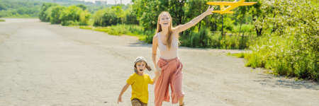 Happy mother and son playing with toy airplane against old runway background. Traveling with kids concept. BANNER, LONG FORMATの写真素材