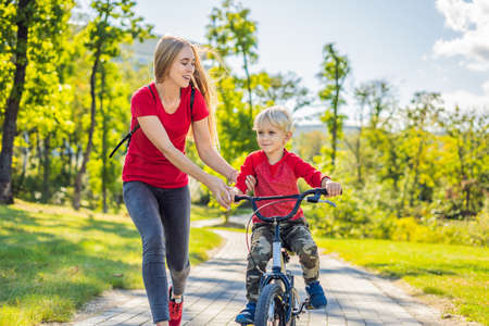 Young mother teaching her son how to ride a bicycle in the parkの写真素材