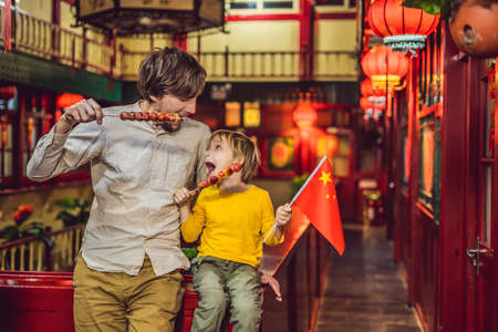 Enjoying vacation in China. Happy tourists dad and son with a Chinese flag and with traditional Chinese candied fruitsの写真素材