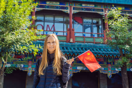 Enjoying vacation in China. Young woman with national chinese flag on the background of the old Chinese street. Travel to China concept.の写真素材