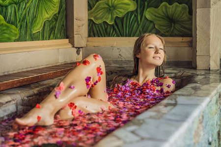 Attractive Young woman in bath with petals of tropical flowers and aroma oils. Spa treatments for skin rejuvenation. Alluring woman in Spa salon. Luxury spa and skin careの写真素材