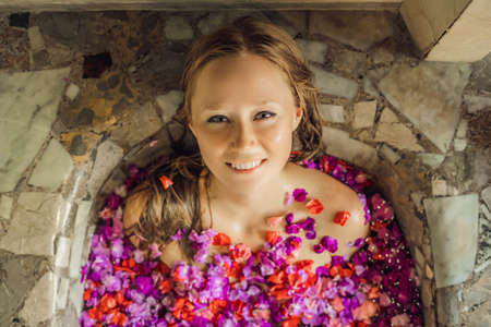 Attractive Young woman in bath with petals of tropical flowers and aroma oils. Spa treatments for skin rejuvenation. Alluring woman in Spa salon. Luxury spa and skin careの写真素材