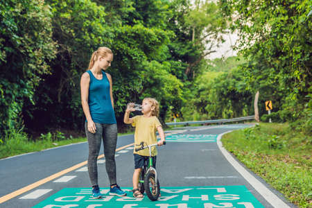 Sporty woman running on road at sunrise. Son goes to balance bike. Fitness and workout wellness conceptの写真素材