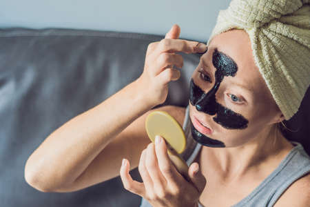 Beautiful young woman relaxing with face mask at home. Happy joyful woman applying black mask on faceの写真素材